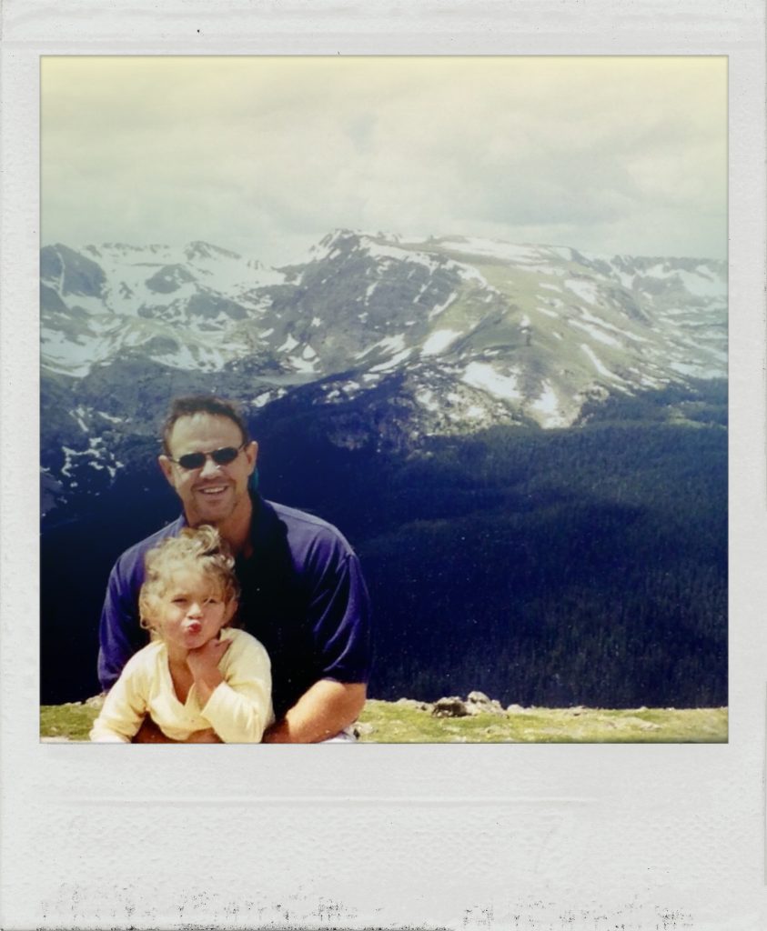 Father and young daughter smile in front of mountains
